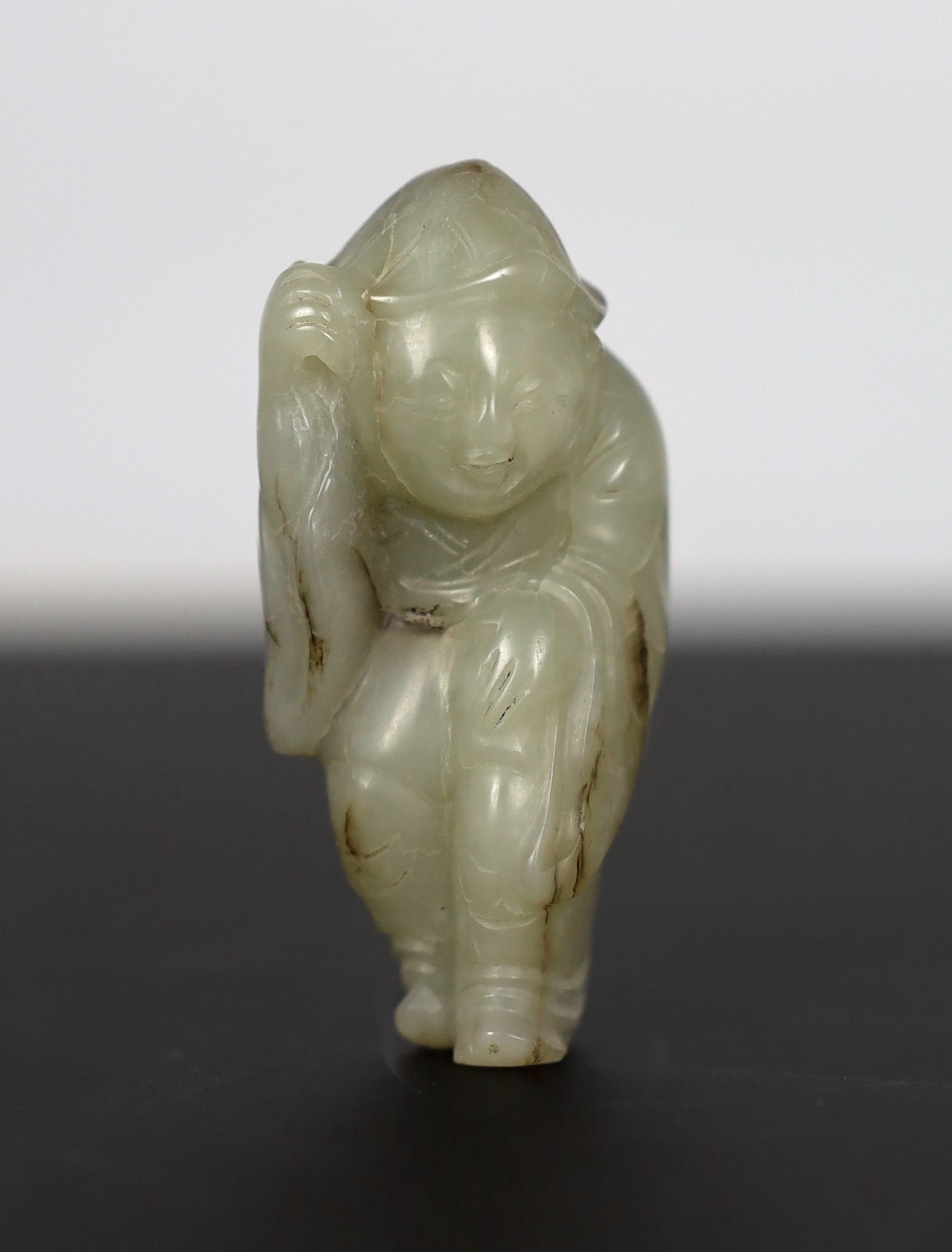 A Chinese white jade figure of a boy wearing a hat and long coat, Ming dynasty